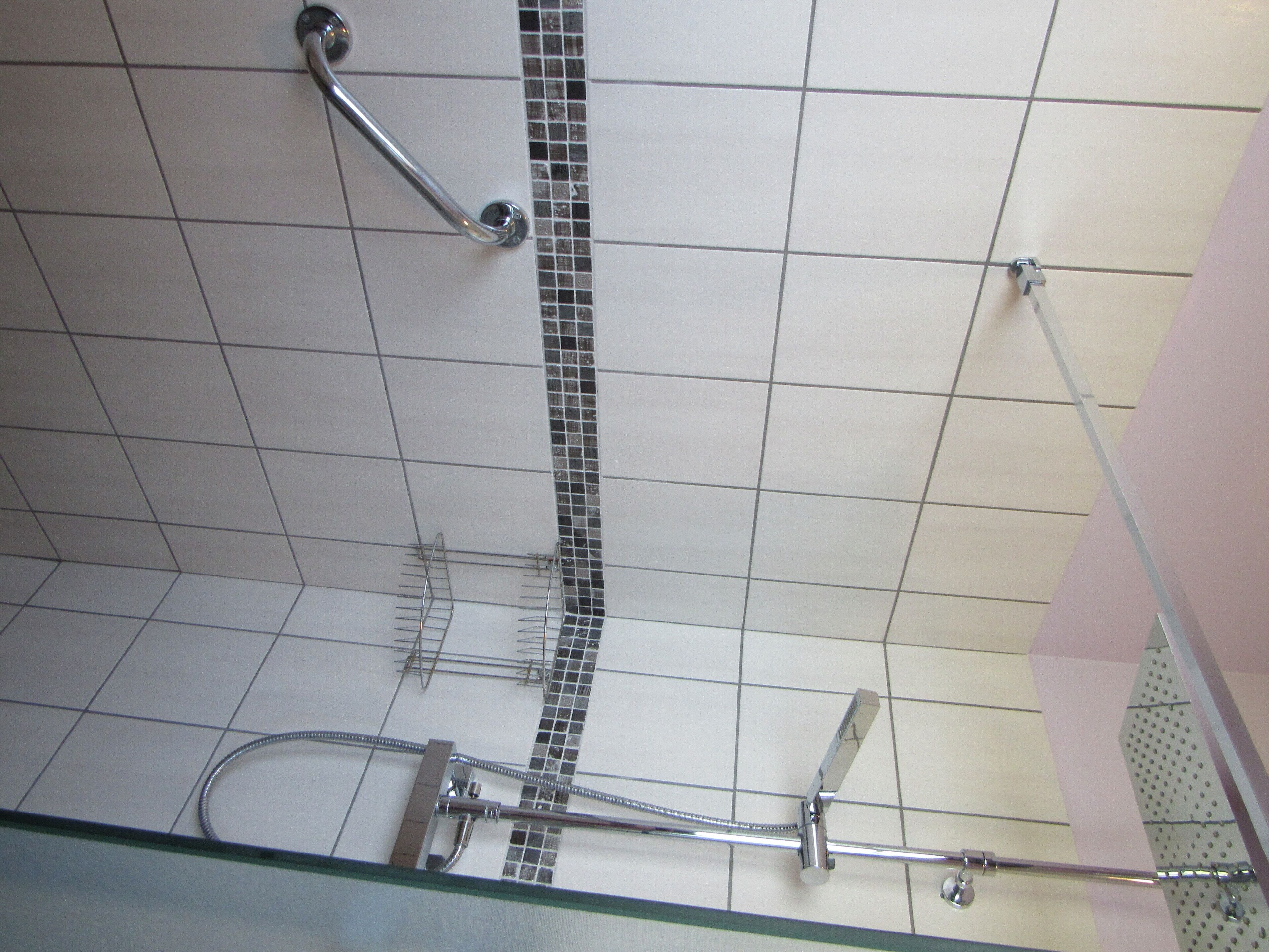 Een badkamer met betegelde vloer, een douche met handgreep en een glazen douchedeur.