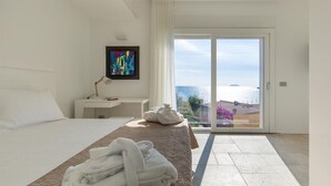 Habitación de hotel con cama, escritorio, televisor y balcón con vista al mar.