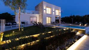 Una casa moderna de dos pisos con piscina, mobiliario exterior y senderos bien iluminados.