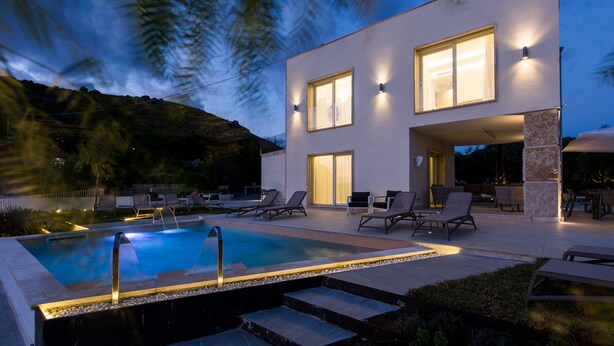 Un edificio moderno de dos pisos con piscina, mobiliario exterior y vistas del paisaje circundante.