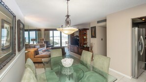 A modern living room with a glass dining table, green chairs, a sofa, and a television. - South Seas Tower 3 1807- Beach Views! (Marco Island)