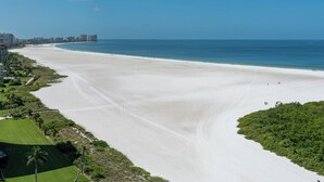 A wide beach with a gentle curve, a clear blue sky, and a distant city skyline. - South Seas Tower 3 1807- Beach Views! (Marco Island)