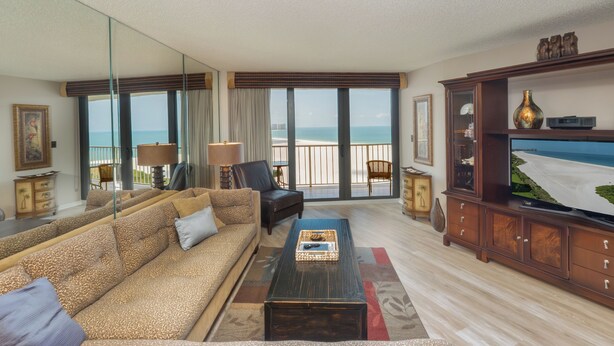 A living room with a sofa, a coffee table, a TV, and a view of the beach. - South Seas Tower 3 1807- Beach Views! (Marco Island)