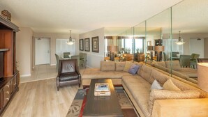 A spacious living room with a large sofa, a coffee table, and a dining area with chairs and a table. - South Seas Tower 3 1807- Beach Views! (Marco Island)