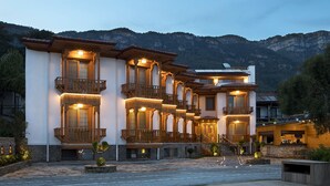 Un hotel de varios pisos con balcones, fachada de piedra y montañas al fondo.