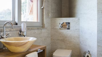 A bathroom with a large vessel sink, a toilet, a towel rack, and a small shelf with a towel.