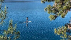 Un lago tranquilo con una persona haciendo paddleboard, rodeado de árboles y colinas al fondo.