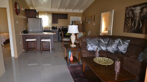 A spacious living area with a brown leather couch, a wooden coffee table, and a kitchen in the background. - Treasure Manor (Ocho Rios)