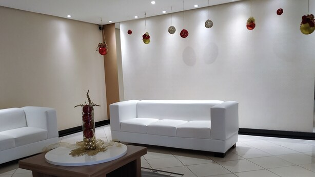 A modern hotel lobby with a white sofa, a round table with a decorative centerpiece, and a wall adorned with hanging ornaments. - Apartment across from UFV with garage. (Centro)