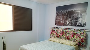 A bedroom with a bed, a window with blinds, a cityscape poster, a potted plant, and a wall socket. - Apartment across from UFV with garage. (Centro)