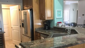 A kitchen with wooden cabinets, a granite countertop, a stainless steel refrigerator, and a coffee maker. - Beautiful, modern home on golf course near South Padre Island (Laguna Vista)
