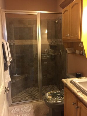 A bathroom with a glass-enclosed shower, a sink with a decorative cover, and wooden cabinets. - Beautiful, modern home on golf course near South Padre Island (Laguna Vista)