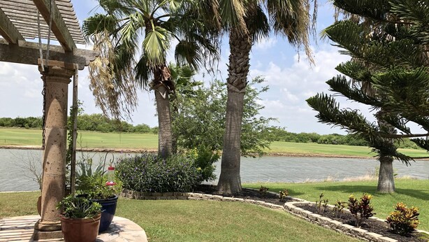 A stone pathway leading to a grassy area with palm trees and a body of water in the background. - Beautiful, modern home on golf course near South Padre Island (Laguna Vista)