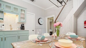 Un comedor con una mesa de madera dispuesta para cuatro personas, rodeada de sillas. Se observa un reloj en la pared y un jarrón con flores sobre la mesa.