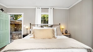 Un dormitorio con una cama grande, dos mesitas de noche con lámparas, una ventana con cortinas y vistas a un espacio exterior.