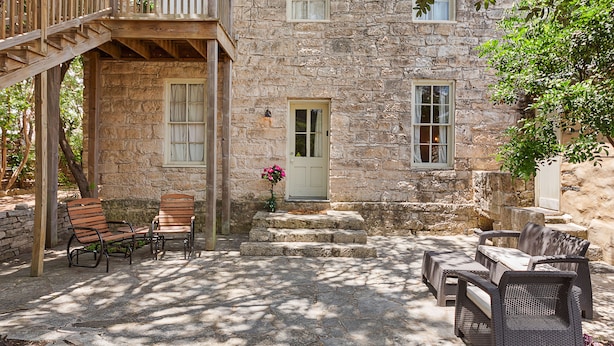 A stone building with a wooden balcony, outdoor seating, and a door with a flower vase. - Itz Inn Back Courtyard Suite | Sleeps 2 | Next to Hondo's On Main Street (Fredericksburg)
