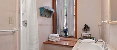 Ein Badezimmer mit einem weißen Waschbecken, einer Holzanrichte, einem Fenster mit Vorhängen und einem Handtuchhalter mit gefalteten Handtüchern.