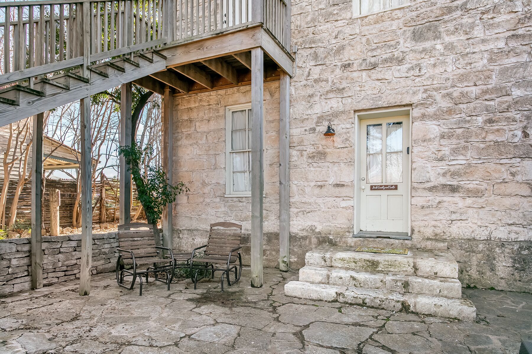 A stone building with a wooden balcony, stone steps, and a door labeled "B&B Cottage Suite".
