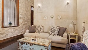 A cozy living room with a stone wall, a beige sofa, patterned cushions, a rustic coffee table, and a small side table with a lamp. - Itz Inn Back Courtyard Suite | Sleeps 2 | Next to Hondo's On Main Street (Fredericksburg)