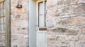 A stone building with a white door, a small wooden step, and a sign that reads "Back Courtyard Suite". - Itz Inn Back Courtyard Suite | Sleeps 2 | Next to Hondo's On Main Street (Fredericksburg)