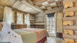 Una cabaña rústica de madera con una cama grande, una ventana con cortinas y una puerta con un panel decorativo.