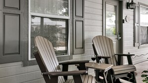 Une véranda avec des fauteuils Adirondack et une table, une porte et une fenêtre donnant sur l’extérieur.