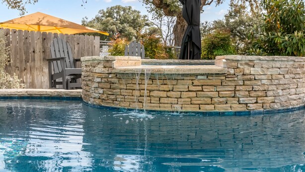 Une piscine avec un mur en pierre et une clôture en bois en arrière-plan.