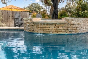 A swimming pool with a stone wall and a wooden fence in the background. - Downtown Retreat Southern Serenity | Walk to Main | Shared Pool & Hot Tub (Fredericksburg)