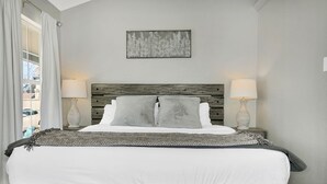 Une chambre avec une tête de lit en bois, deux lampes de chevet, un plaid à motifs et une œuvre d’art florale encadrée accrochée au mur.