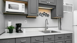 Une cuisine moderne avec des meubles gris, un plan de travail blanc, un évier en acier inoxydable, une machine à café, un four à micro-ondes et un climatiseur fixé au mur.