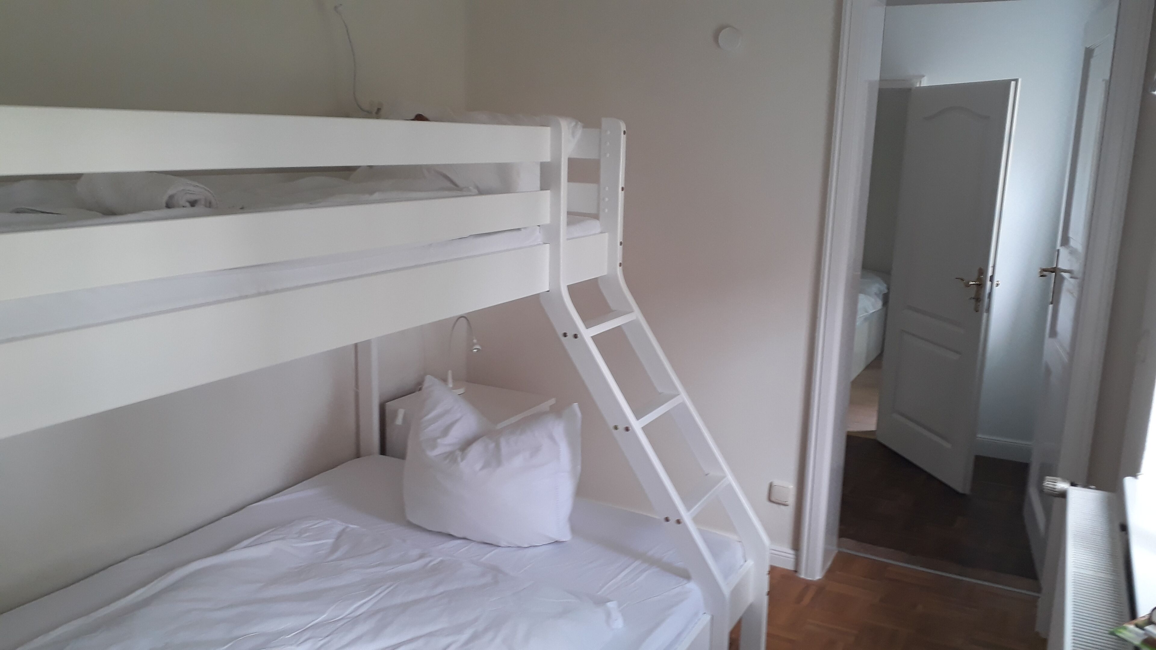 Un lit superposé avec une échelle, un oreiller et une porte donnant sur une autre pièce.