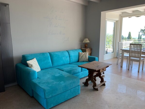 Un salon lumineux avec un canapé bleu, une table basse en bois et une vue sur l’extérieur.
