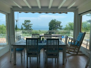 Un espace extérieur abrité, aménagé pour prendre les repas, avec une table et des chaises, offrant une vue panoramique sur la mer et la verdure.