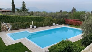 A rectangular swimming pool with a tiled deck, surrounded by well-maintained hedges and a grassy lawn.