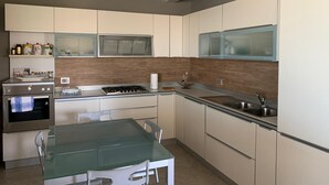 A modern kitchen with a gas stove, a sink, and a dining area with a glass table and chairs.