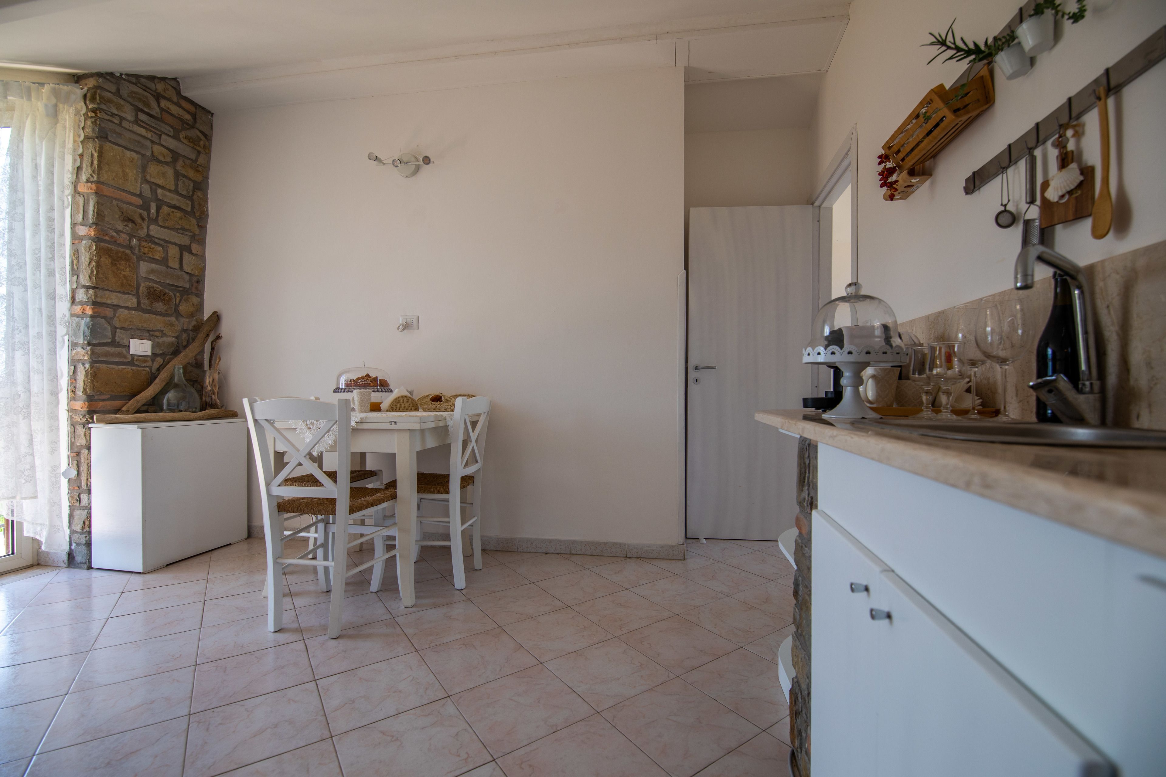 A kitchen with white cabinets, a stone wall, and a dining area with a white table and chairs.