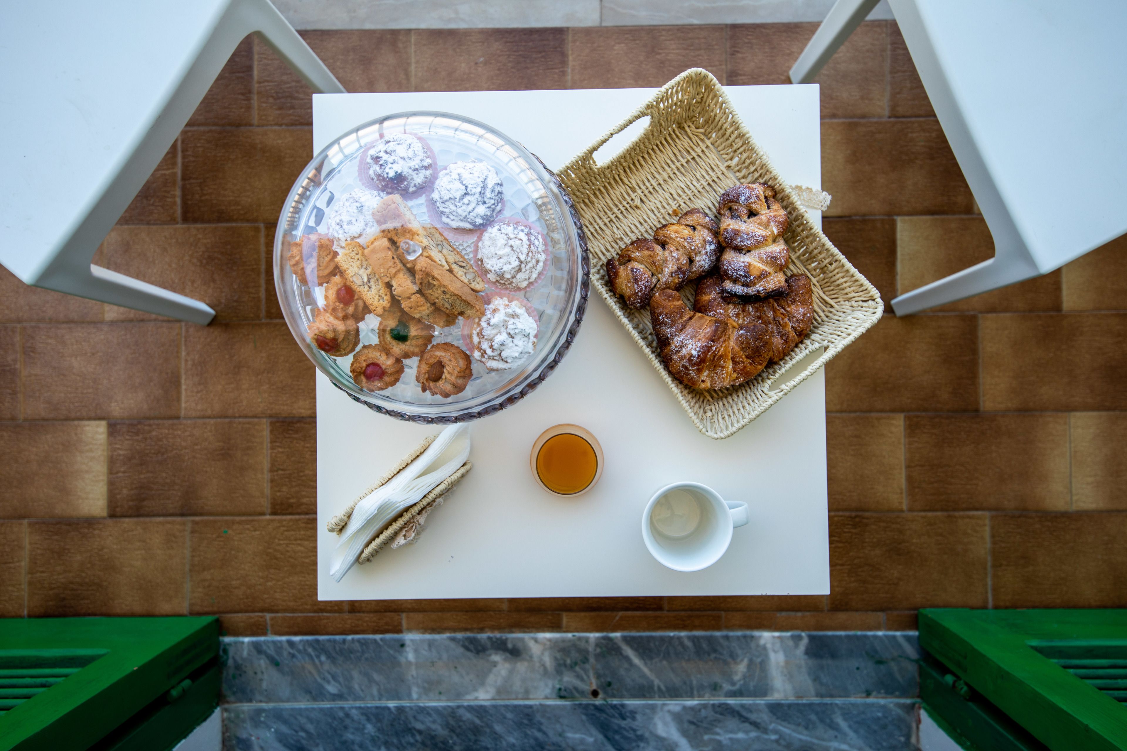 Une table avec un saladier en verre rempli de viennoiseries, un panier de croissants, une tasse de thé et une tasse blanche.