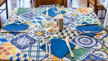 A table set with blue napkins, silverware, and clear glasses, covered by a colorful patterned tablecloth.