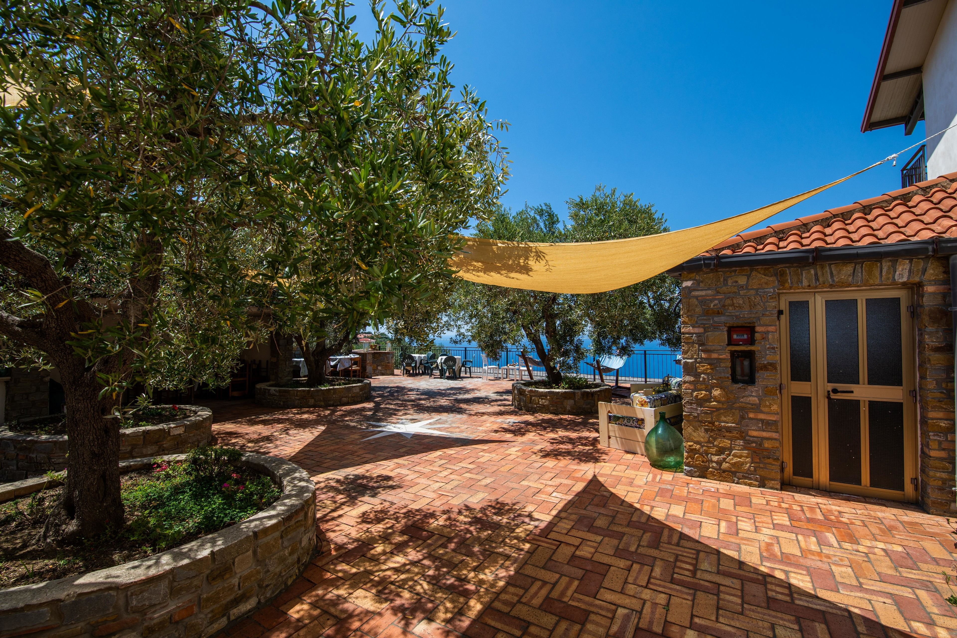 A courtyard with a stone wall, a yellow canopy, and a view of the sea.