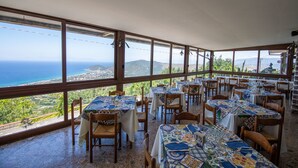 A restaurant with large windows offering ocean views, wooden tables with patterned tablecloths, and a tiled floor. - Hotel Ristorante Madonna Della Scala (Castellabate)