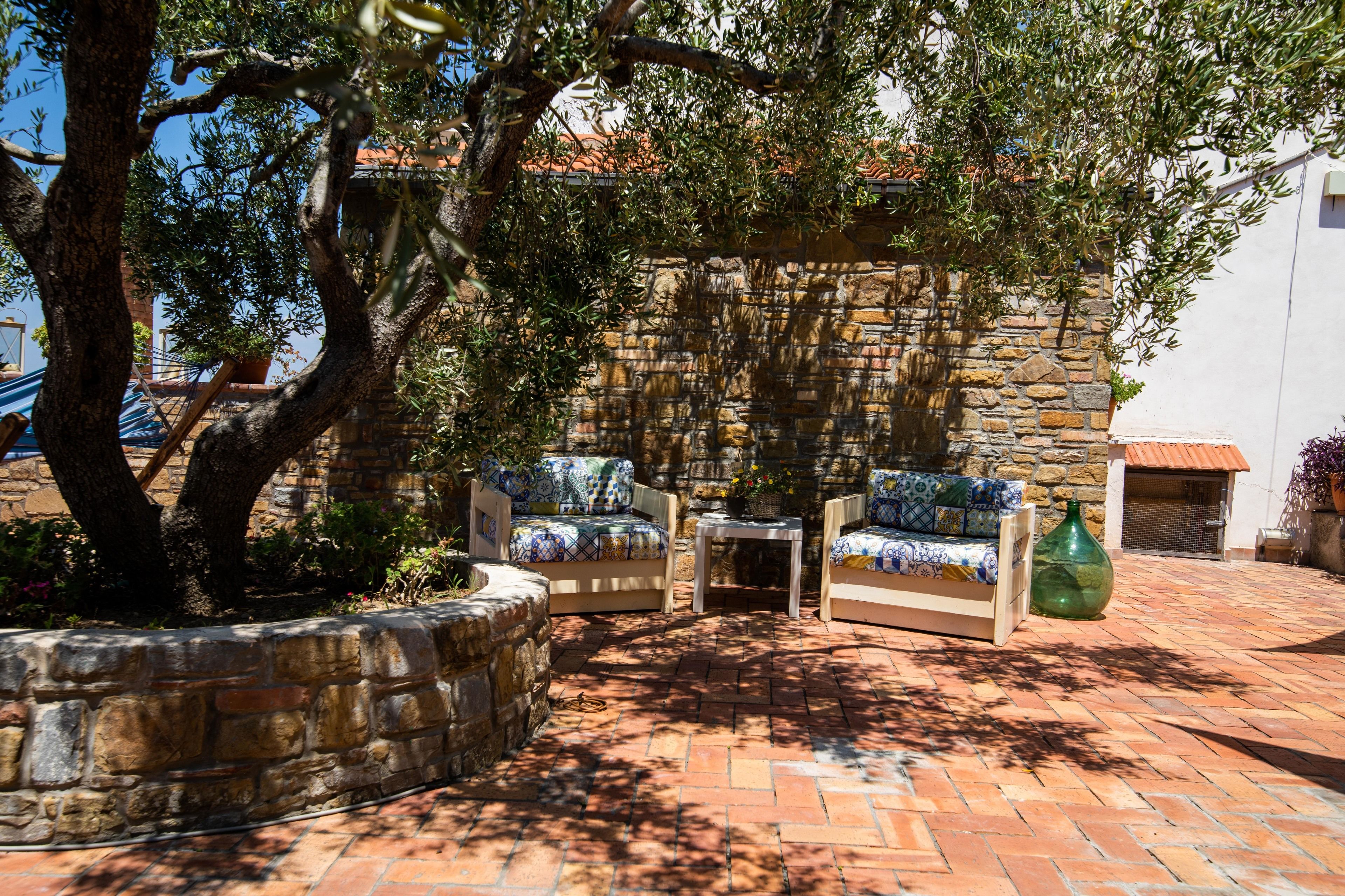 An outdoor seating area with stone walls, a tree, and a tiled floor.