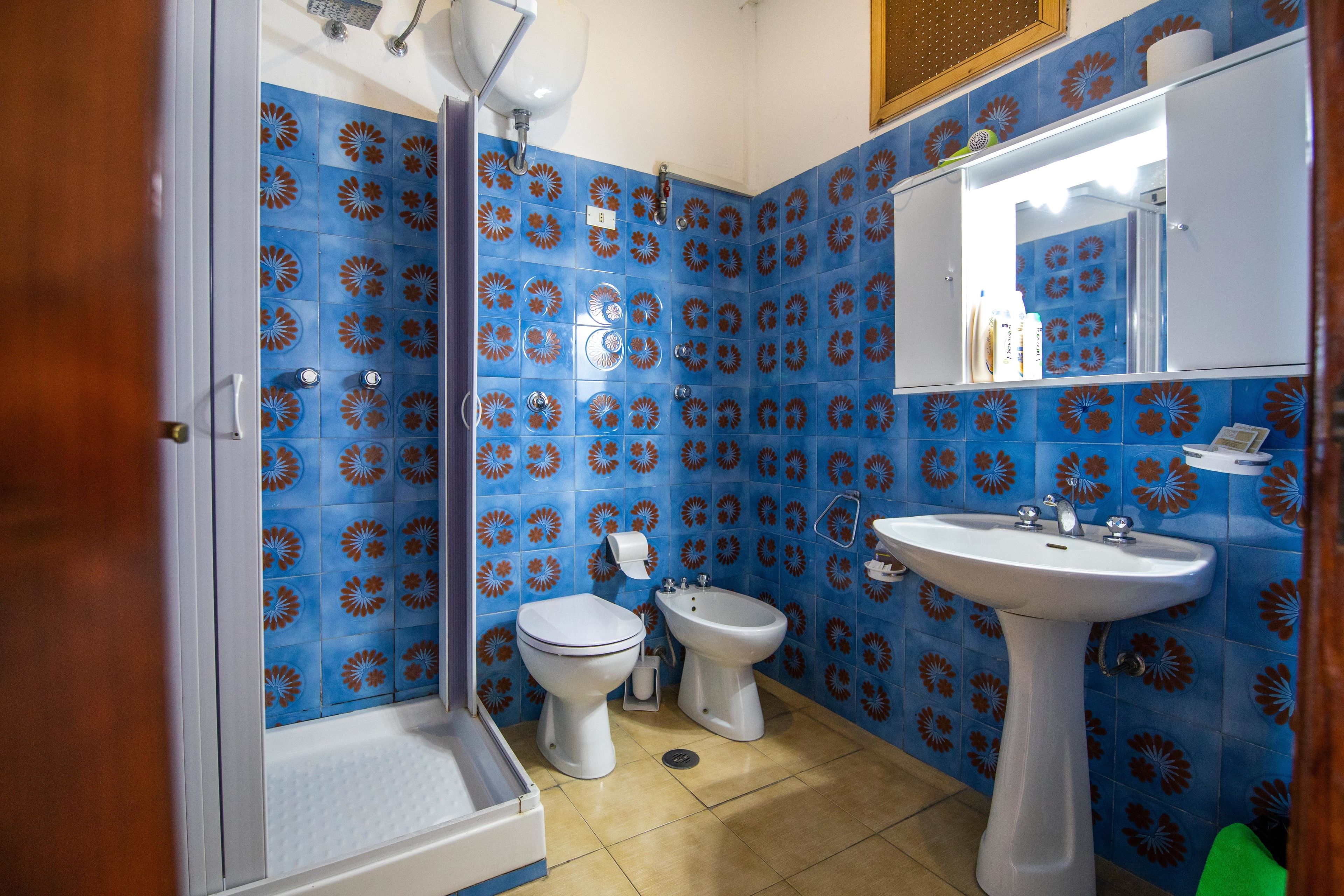 A bathroom with blue and orange floral tiles, a white sink, a white toilet, and a bidet.