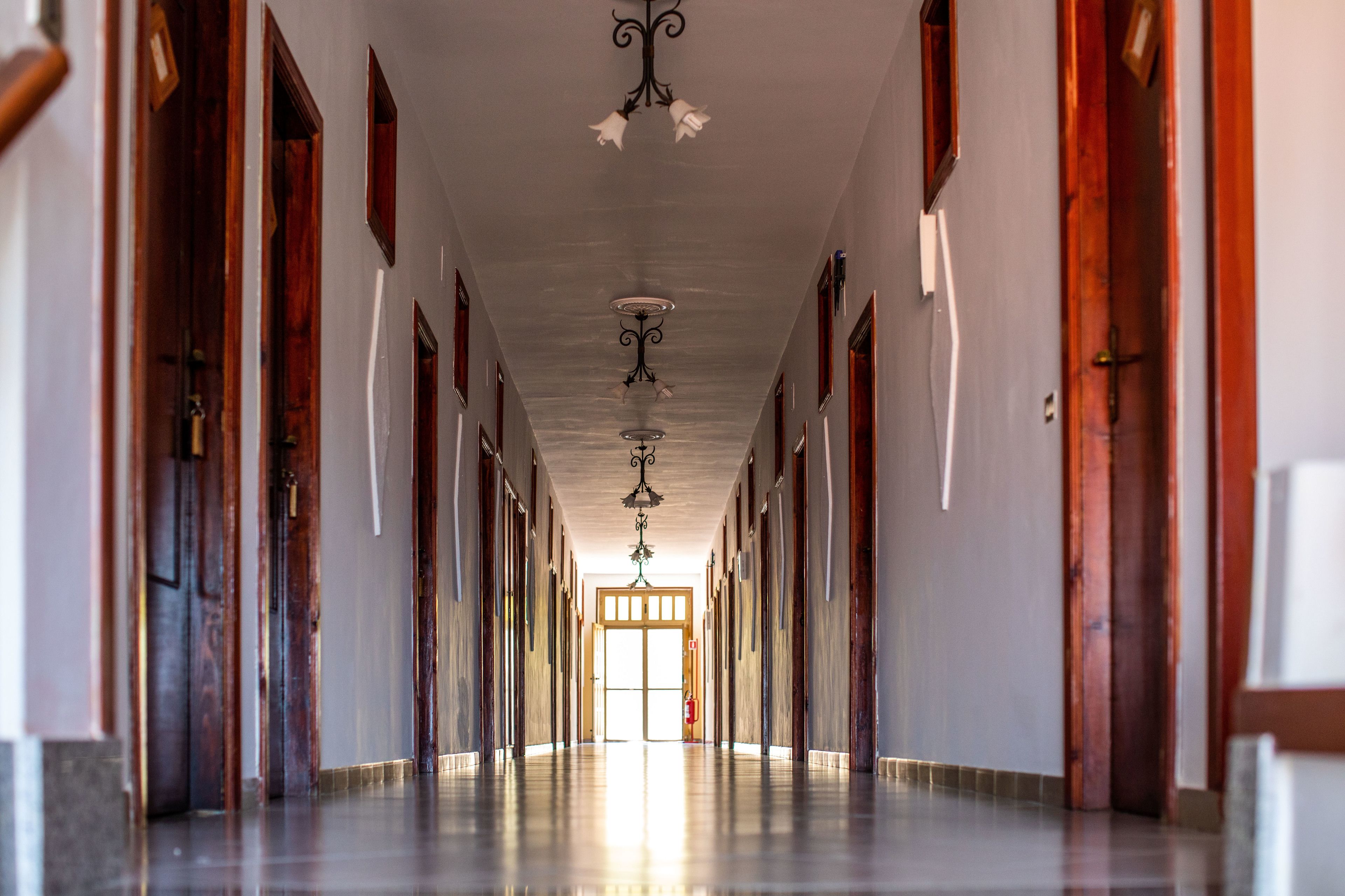 A long, narrow hallway with wooden doors on both sides, a polished floor, and a ceiling with decorative fixtures.