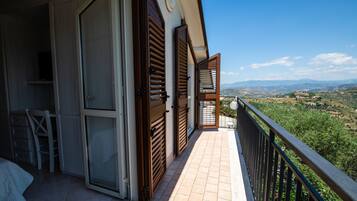A balcony with wooden shutters, a tiled floor, and a view of a hilly landscape.