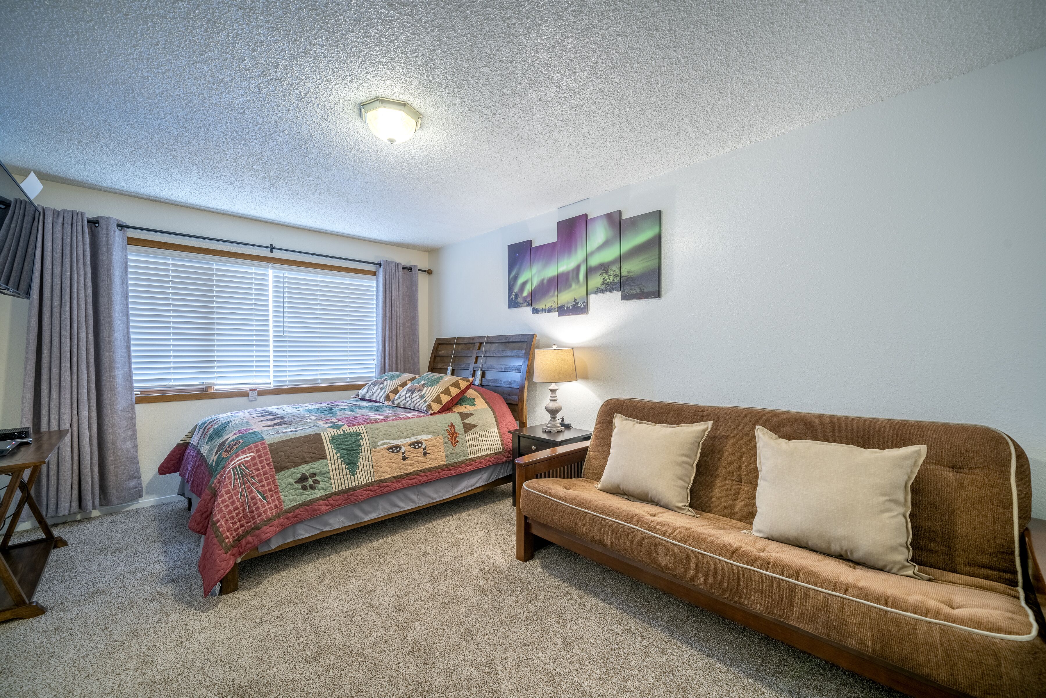 A bedroom with a bed, a sofa, a desk, and a window with curtains.