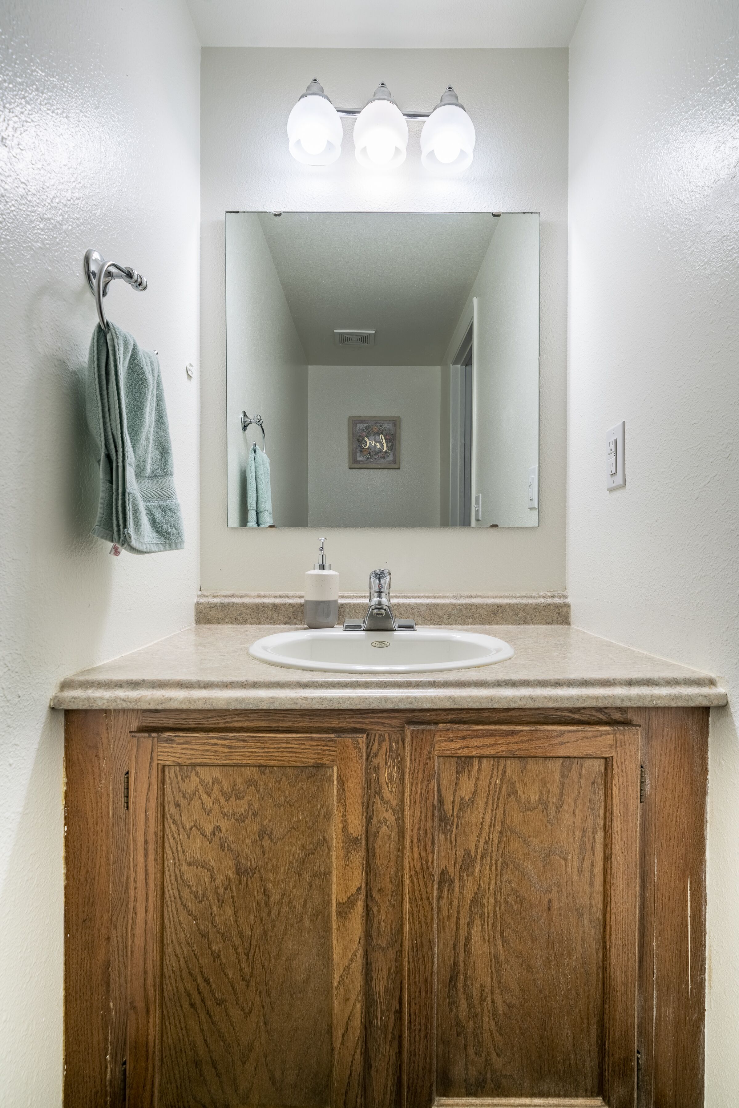 Une salle de bain avec un meuble-lavabo en bois, un lavabo blanc et un miroir doté de trois lampes.