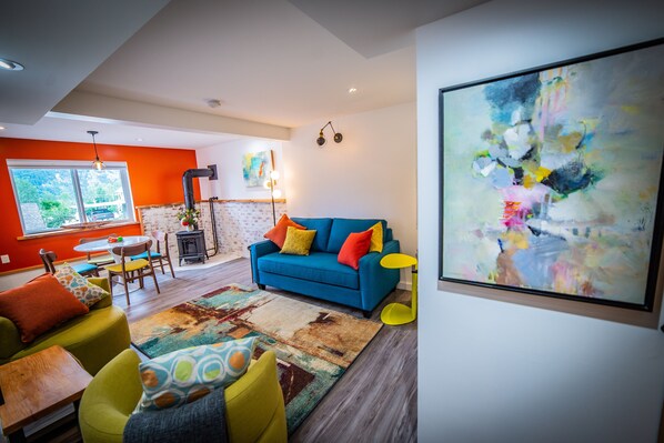 Un salon moderne avec un canapé bleu, des coussins jaunes et orange, un tapis coloré et un grand tableau abstrait accroché au mur.