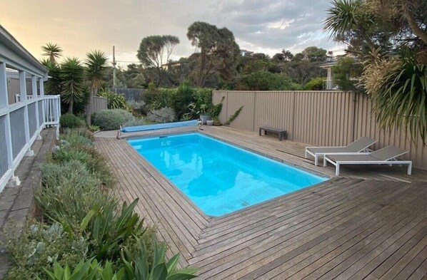 A rectangular swimming pool with a wooden deck, surrounded by greenery and a wooden fence. - FABULOUS FOAM COASTAL HOLIDAY HOME, SOLAR POOL & ENTERTAINER, BLAIRGOWRIE (Blairgowrie)