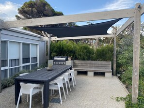 An outdoor patio with a wooden table and white chairs, a barbecue grill, and a wooden bench. - FABULOUS FOAM COASTAL HOLIDAY HOME, SOLAR POOL & ENTERTAINER, BLAIRGOWRIE (Blairgowrie)
