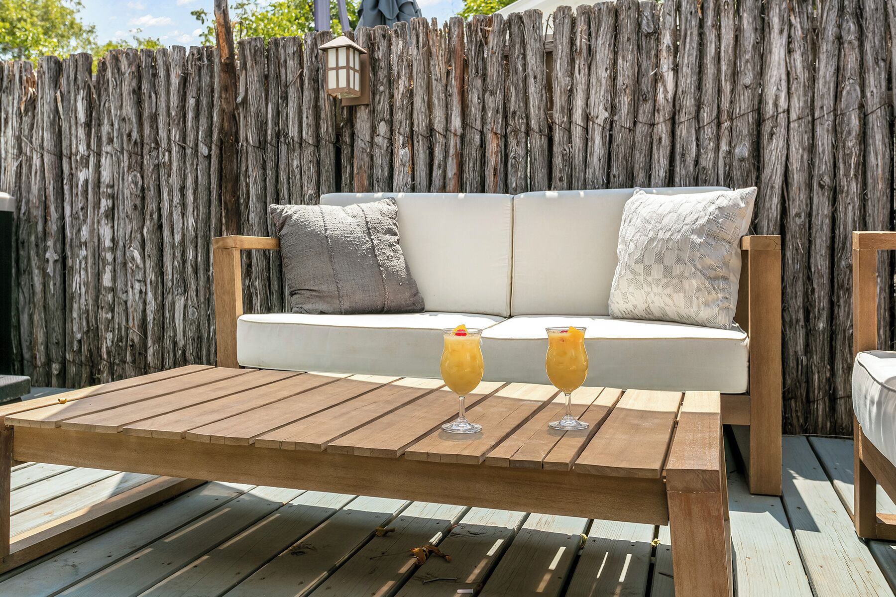 Eine Holzterrasse mit einem weißen Sofa und zwei Gläsern Orangensaft.